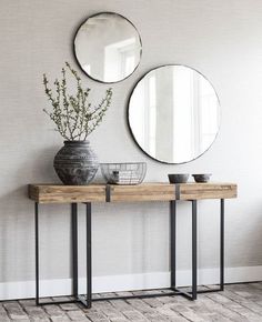 two round mirrors are hanging on the wall above a table with vases and plants