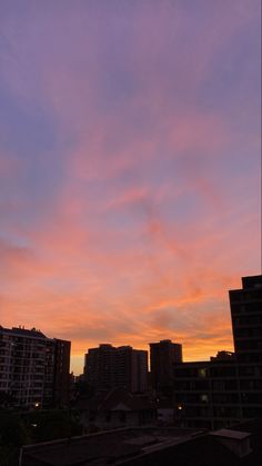 the sky is pink and purple as it sets over some buildings in an urban area