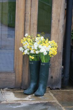 flowers in green rubber boots are sitting on the ground next to an open wooden door