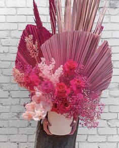 a vase filled with lots of pink flowers on top of a wooden table next to a brick wall