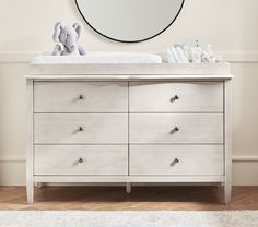 a baby crib with a mirror and teddy bear on the dresser in front of it