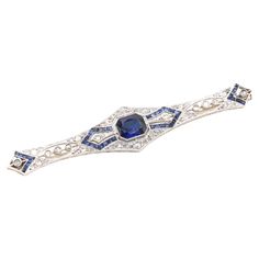 An Art Deco sapphire, diamond, white gold, and platinum brooch, comprising one large octagonal cut sapphire, forty-four calibre cut sapphires, and fifty-two rose cut diamonds, set in platinum, backed in 18 karat white gold, with 18 karat white gold pin and fittings. This stunning brooch is set to the centre with a large octagonal cut sapphire. The sapphire is a deep, vibrant blue, and is held within a platinum setting with millegrain edging, which appears as if floating. To either side of the central sapphire, a pair of rose cut diamonds are held within kite shapes, the shape echoed by a border of calibre cut sapphires. Glittering rose cut diamonds stud the brooch, with 3 bezel set diamonds held within a marquise shape to each side. Arrow shapes set with calibre cut sapphires encases the f Vintage Sapphire Brooches As Gift, Diamond Gemstone Brooches In Art Deco Style, Art Deco Diamond Hallmarked Brooches, Art Deco Diamond Brooches With Gemstone, Art Deco Diamond Brooch, Lalique Jewelry, Art Deco 1920s, Gold Pin, Bezel Set Diamond