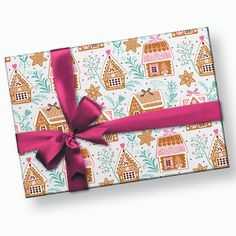 a wrapped gift box with a pink ribbon and gingerbread houses on the wrapping paper