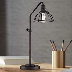 a desk lamp sitting on top of a wooden table next to a pen holder and pencils