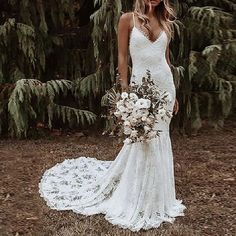 a woman in a white wedding dress standing next to some trees and holding a bouquet