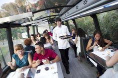 a group of people sitting at tables inside of a bus with food on the table