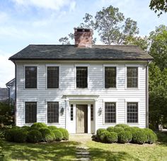 a white two story house with black shutters on the front and side windows, surrounded by green grass