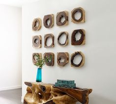 a wooden table topped with a blue vase filled with green plant sitting next to a white wall