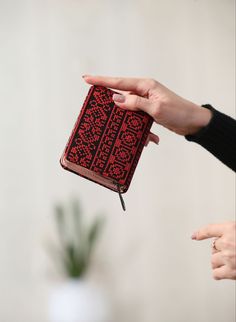 two hands holding a red and black book with writing on the cover, while another hand points at it