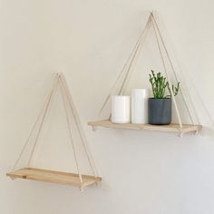 two wooden shelves with plants and candles on them hanging from the wall in a white room