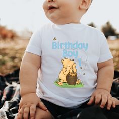 a baby sitting on the ground wearing a winnie the pooh birthday shirt