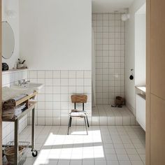 a white tiled bathroom with a chair in the corner and a mirror on the wall