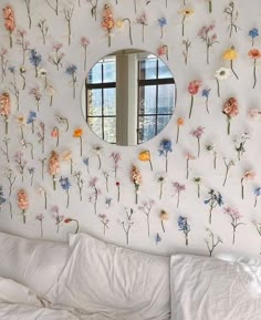 a bedroom with flowers on the wall and a round mirror above it's bed