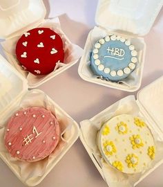 four decorated cakes in plastic containers on a table