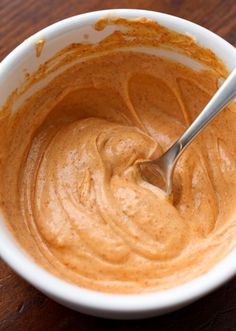 a white bowl filled with peanut butter on top of a wooden table next to a spoon