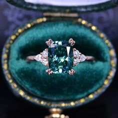 an emerald colored ring in a velvet box with gold trimmings and diamond accents