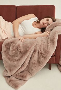 a woman laying on a couch covered in a blanket