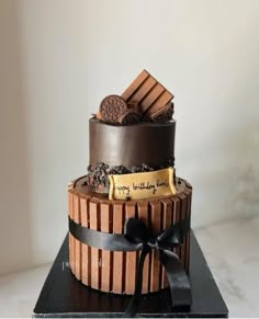 a three tiered chocolate birthday cake with cookies on top and ribbon around the edges