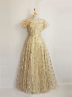 This gold silk and tulle gown would make a stunning alternative wedding dress or a decadent evening gown. The under layer is a luxurious pale gold silk dupion and the overlay is a featherlight art deco rose printed tulle. It can also be made in a shorter length for a 1950s vintage style dress.  It features a high necked version of our Bustier Grace bodice, with an illusion neckline and a keyhole opening at the back. The gently flared silhouette of the silk underlayer is then complemented by the Champagne Tulle Gown For Gala, Elegant Gold Tulle Evening Dress, Ethereal Tulle Evening Dress For Wedding, Champagne Tulle Evening Dress, Ethereal Gown With Sheer Bodice For Party, Gold Tulle Gown For Gala, Gold Tulle Evening Dress For Formal Occasions, Ethereal Floor-length Evening Dress For Prom, Ethereal Ball Gown For Wedding