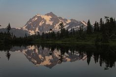 a mountain is reflected in the still water of a lake with pine trees on both sides