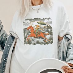 Get ready to show your style with our Retro Cowgirl Lasso T-Shirt! Perfect for a beach party, concert or or just a casual day out, this graphic tee is a must-have.  Proudly Printed on Comfort Colors® tees, for that insanely soft, vintage look and feel.  Without doubt, this will be your favorite shirt. With its vintage-inspired design, this shirt is perfect for those who love a boho, western, or retro look. The oversized fit and soft, comfortable fabric make it the perfect choice for a day on the Fun Short Sleeve T-shirt For Music Festival, Summer Pop Culture Crew Neck Shirt, Pop Culture Sublimation Print T-shirt For Summer, White Pop Culture Shirt For Summer, Summer Pop Culture Graphic Print Shirt, Summer Pop Culture Tops With Funny Print, Pop Culture Screen Print Tops For Summer, Summer Pop Culture Top With Funny Print, Pop Culture Funny Print Summer Top