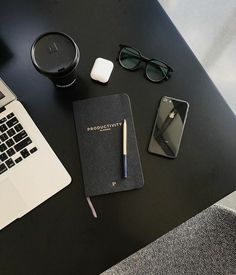 a laptop computer sitting on top of a desk next to a notebook and pen with glasses