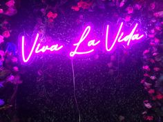 a purple neon sign that says vera la vie on it in front of some flowers