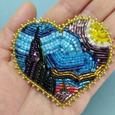 a hand holding a heart shaped beaded brooch