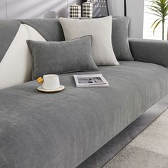 a gray couch with pillows and a cup on the arm rest in front of it