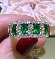 a woman's hand holding a ring with three emeralds and diamonds on it