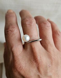 Add a touch of elegance and contemporary flair to your jewelry collection with the freshwater white pearl modern contempo ring. This striking open ring features one all natural freshwater button pearl with a smooth surface. The setting's modern contempo style is an open S925 sterling silver band that allows for an adjustable fit and a contemporary aesthetic. Open accommodates various finger sizes and adds a unique touch.  Pictures may reflect a close up view to ensure you have an accurate and de Modern Pearl Wedding Ring, Modern Pearl Ring For Formal Occasions, Modern Pearl Rings For Anniversary, Modern Pearl Open Ring For Anniversary, Modern Open Pearl Ring For Anniversary, Modern Everyday Pearl Ring, Classic Everyday White Gold Pearl Ring, Sterling Silver White Gold Pearl Ring With Pearl Drop, Open Pearl Ring With Pearl Drop