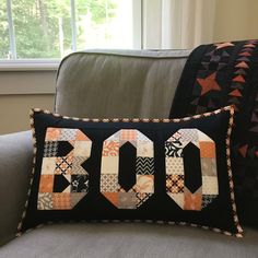 a black pillow with the word boo on it sitting next to a gray couch in front of a window