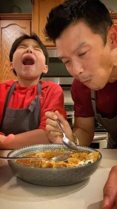 a man and boy are looking at a bowl of food with spoons in it