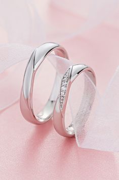 two white gold wedding rings with diamonds on pink satine background, close - up