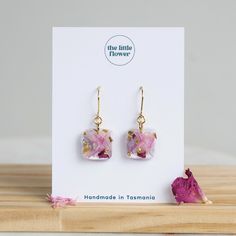 the little flower earrings are made with pink flowers and gold leaf accents, on top of a card