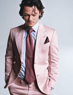 a man in a pink suit and tie is posing for a photo with his hands in his pockets