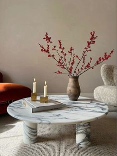 a marble coffee table with candles and flowers on it in front of a red chair