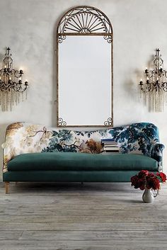 a blue couch sitting in front of a mirror on top of a wooden floor next to a vase with flowers