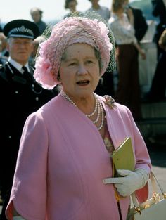 an older woman wearing a pink hat and holding a book in her hand while standing next to other people