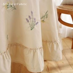 the back of a chair with a white table cloth on it and some purple flowers