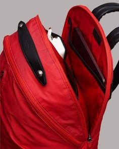 an open red backpack with ear buds in it's pocket and zippers on the side