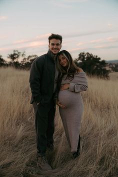 a pregnant couple standing in tall grass at sunset