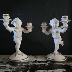 two white figurines holding trays on top of each other in front of a black background