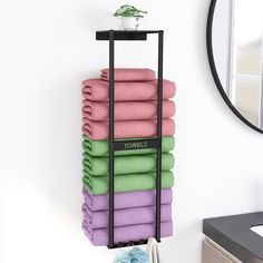 towels are stacked on a towel rack in front of a mirror and wall with a potted plant