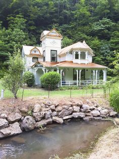 a large white house sitting on top of a lush green hillside next to a river