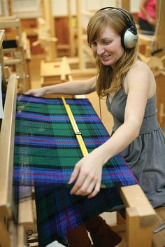 a woman wearing headphones is working on a weaving project with a large piece of fabric