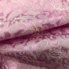 pink and white brocaded fabric with an intricate design on the bottom, along with a gold monogrammed logo