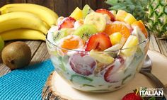 a fruit salad in a glass bowl on top of a wooden table next to pineapples