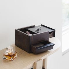 a wooden box with two rings on it sitting on a table next to a bottle of perfume