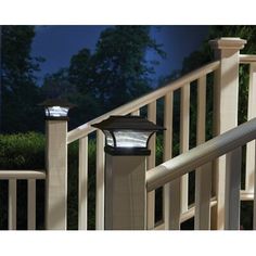 an outdoor light on the side of a wooden deck next to a white railing with trees and bushes in the background